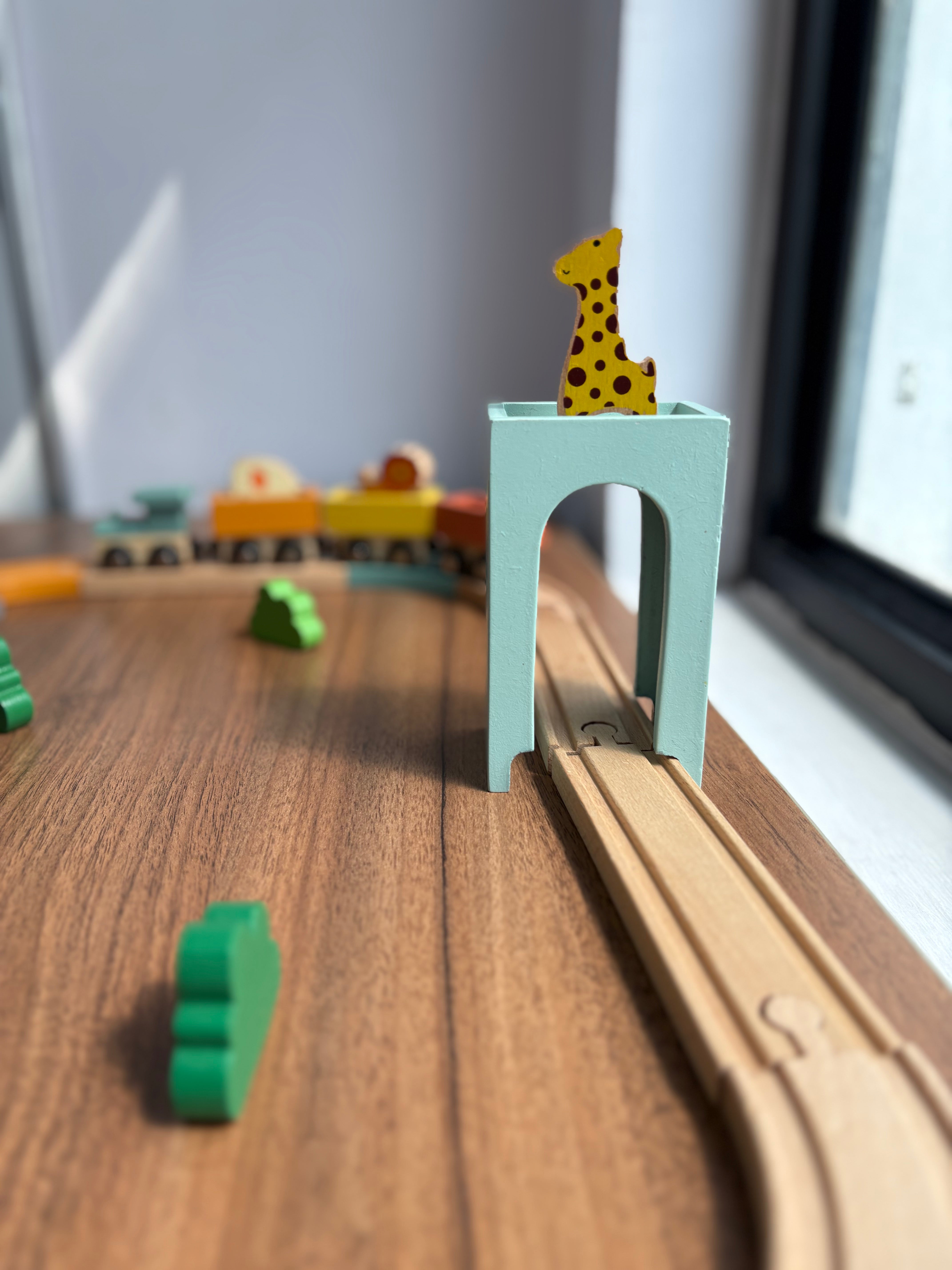 Wooden toy train set with a giraffe figurine on a small bridge