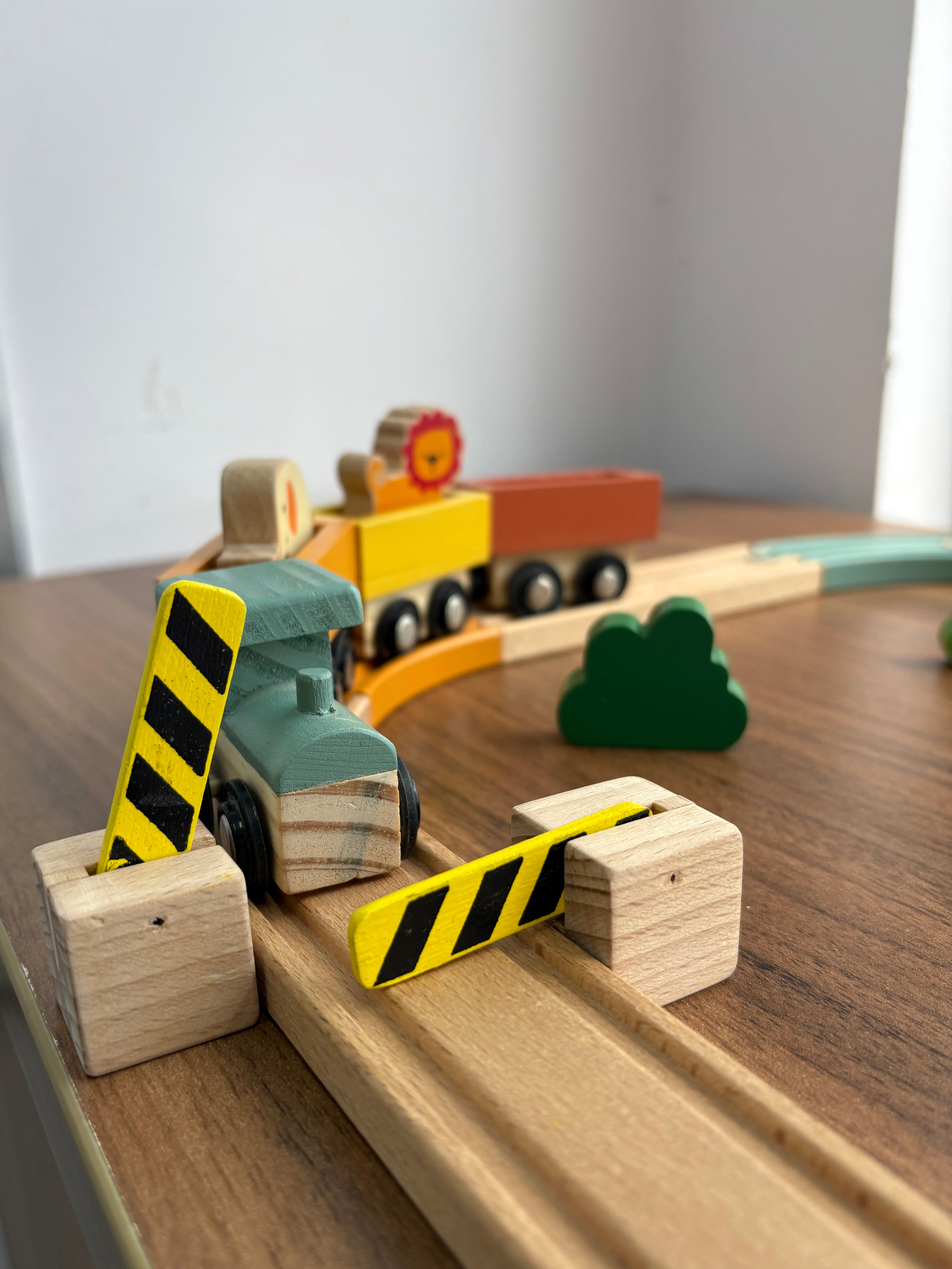 Wooden toy train set on a wooden surface with a white wall background